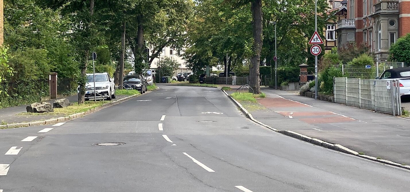 Eine breite, asphaltierte Straße mit einem Fahrradpiktogramm, dass die Fahrbahn von außen zur mitte hin bedeckt.